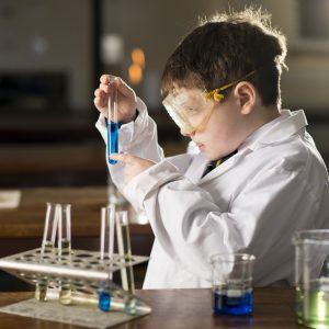 child in lab coat holding up test tubes next to a bunsen burner